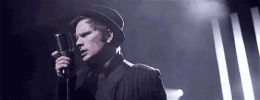 a man wearing a hat is singing into a microphone on a stage .