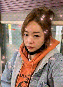 a woman wearing an orange hoodie and a denim jacket taking a selfie