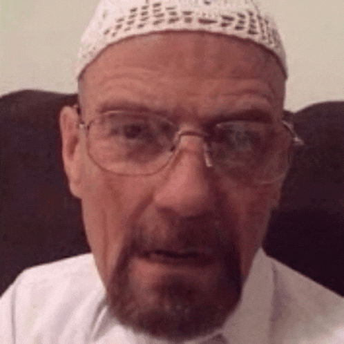 a man with a beard and glasses is wearing a white hat and a white shirt .