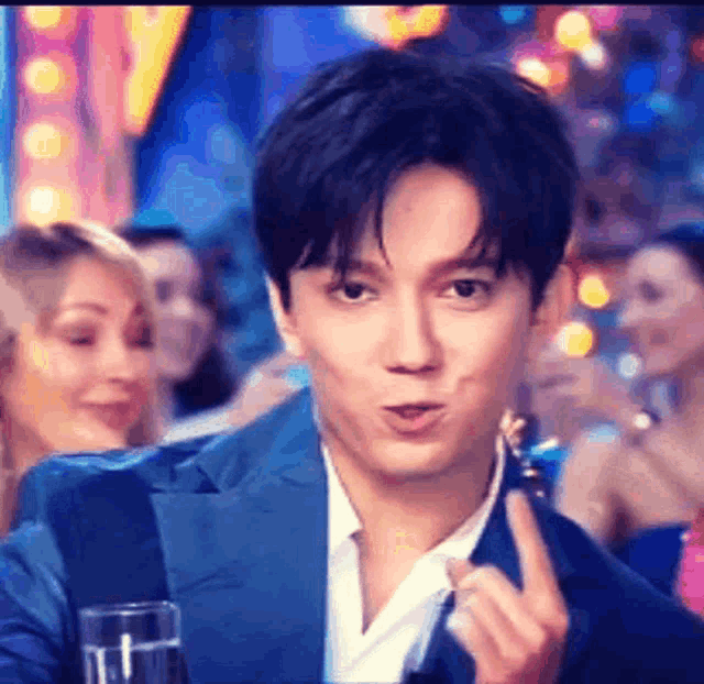 a man in a blue suit and white shirt is making a funny face while holding a glass of water .