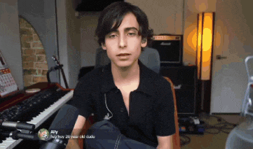 a young man in a black shirt is sitting in front of a keyboard and a microphone with ally written on the screen