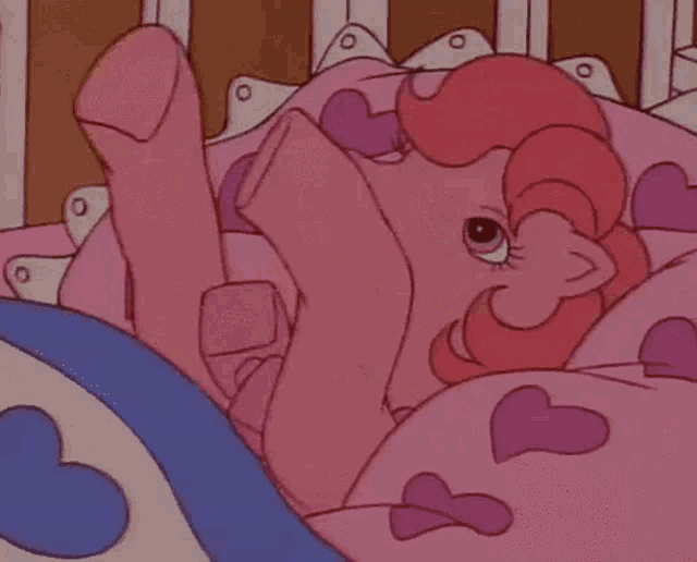 a cartoon girl is sleeping in a bed with a teddy bear and hearts on the sheets .