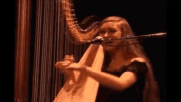 a woman in a black dress is playing a harp and singing into a microphone .