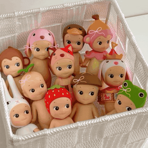 a bunch of dolls in a basket including one with a strawberry hat on