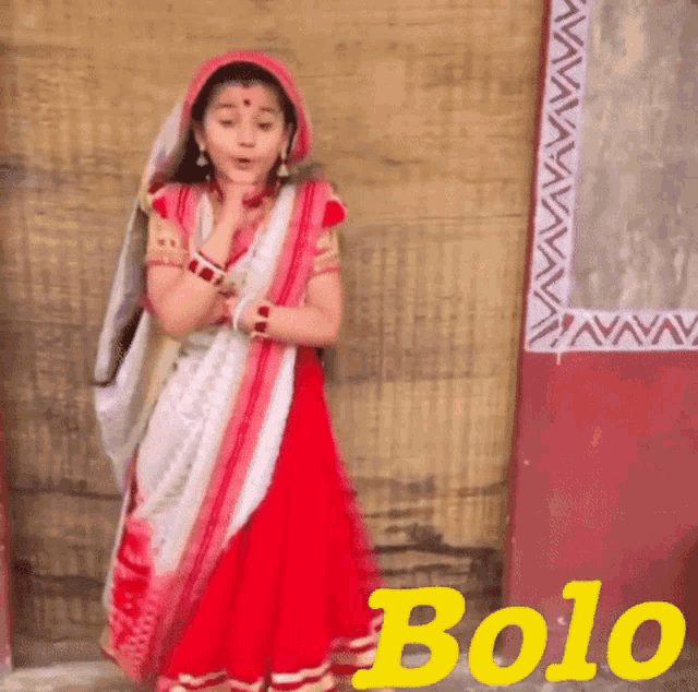a little girl in a red and white dress is standing in front of a wall that says bolo on it .