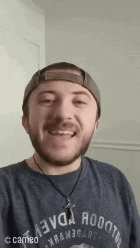 a man with a beard wearing a hat and a necklace is smiling for the camera .