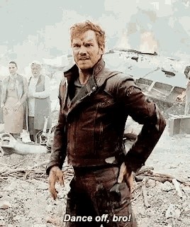a man in a leather jacket is standing in a field with his hands on his hips and saying `` dance off , bro ! ''