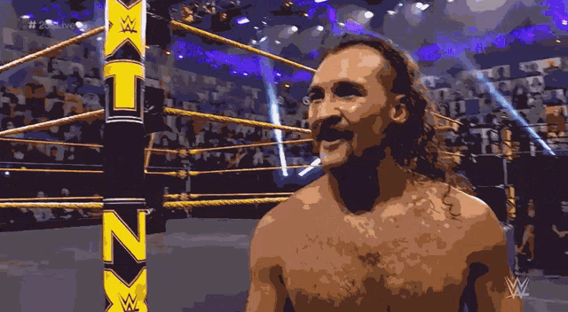 a shirtless wrestler in a wrestling ring with the letters nxt in the background