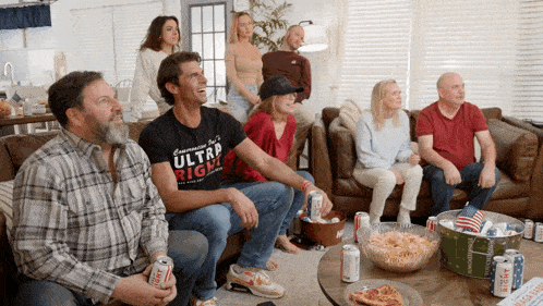 a group of people are sitting on a couch watching a game and one man is wearing a shirt that says ultra right