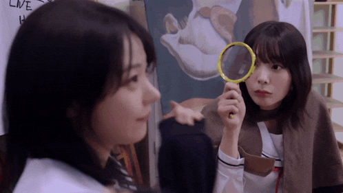 a girl holding a magnifying glass looks at another girl 's face