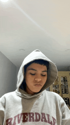 a young man wearing a riverdale hoodie looks down at something
