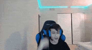 a young man wearing headphones and a microphone is sitting in a gaming chair .