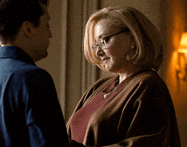 a woman wearing glasses looks at a man in a blue shirt