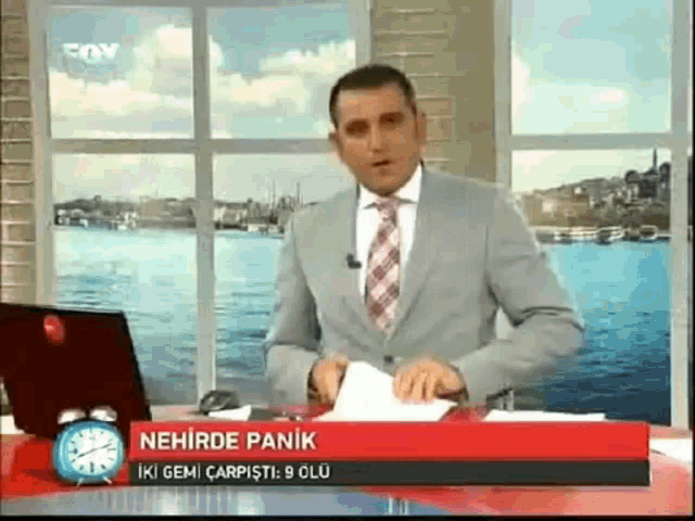 a man in a suit and tie is holding a piece of paper in front of a sign that says nehirde panik