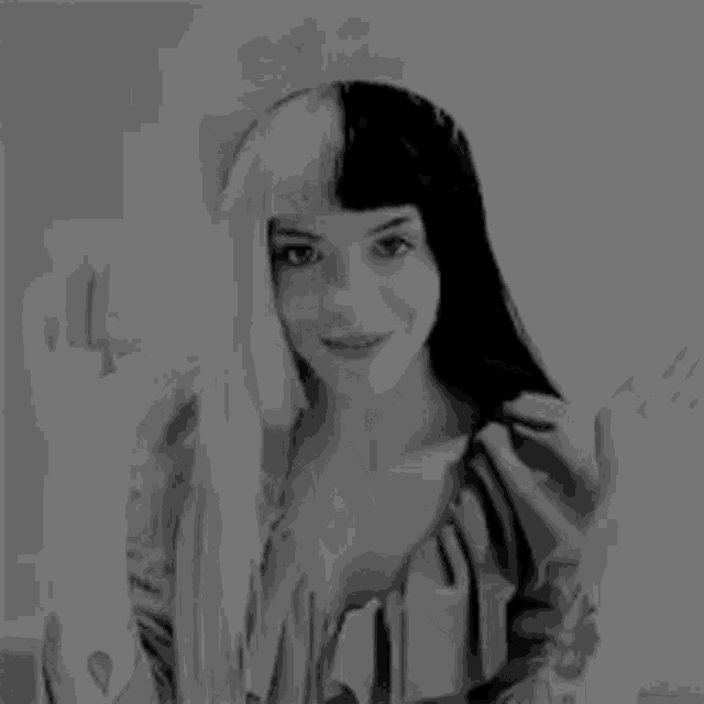 a black and white photo of a woman with half black and half white hair waving at the camera .