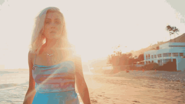 a woman in a blue dress stands on the beach at sunset