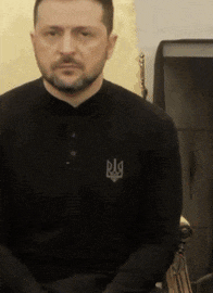a man with a beard is wearing a black shirt with the letter r on the front