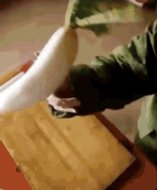 a person in a green jacket is cutting a vegetable on a wooden cutting board