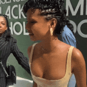 a woman in a yellow tank top stands in front of a green wall that says black hollywood