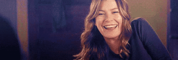 a woman is smiling and laughing while sitting at a table in a dark room .