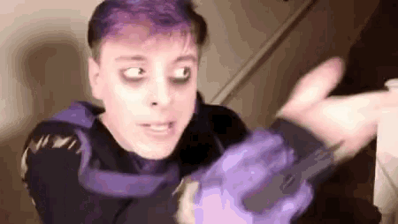 a man with purple hair and black eyes is holding a purple object in his hand .
