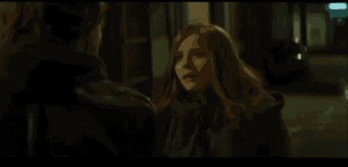 a woman is standing next to a man in a dark room and they are looking at each other .