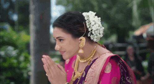 a woman in a pink and purple saree with a flower in her hair is smiling .