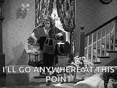 a black and white photo of a woman standing in a living room holding a dog .