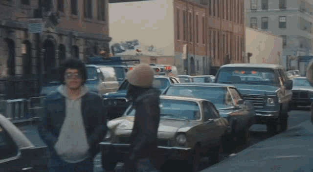 a group of people standing on a street with cars parked on the side of the road