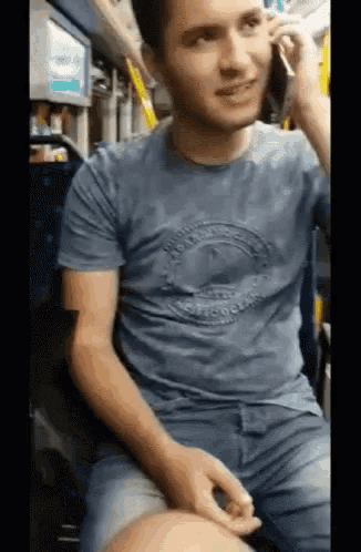 a man in a blue shirt is talking on a cell phone on a bus