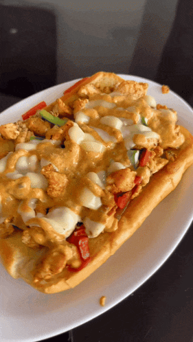 a white plate topped with a sub sandwich with chicken cheese and peppers
