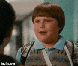 a young boy with a backpack is talking to another boy in a hallway .