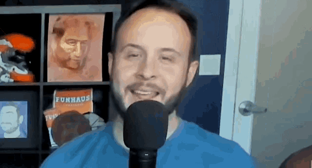 a man with a beard is smiling while holding a microphone in front of a shelf with a funhaus book on it