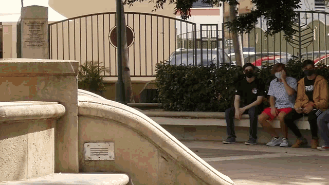a group of people wearing face masks sit on a bench in front of a fence with a plaque on it