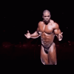 a muscular man in a bikini is dancing on a stage in the dark .