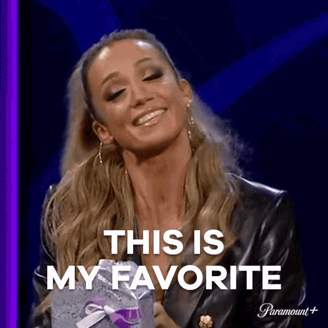 a woman in a black leather jacket is holding a gift box and smiling while saying this is my favorite .