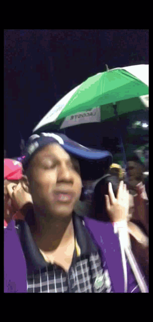 a man wearing a blue hat stands in front of a green umbrella that says ' toyota ' on it