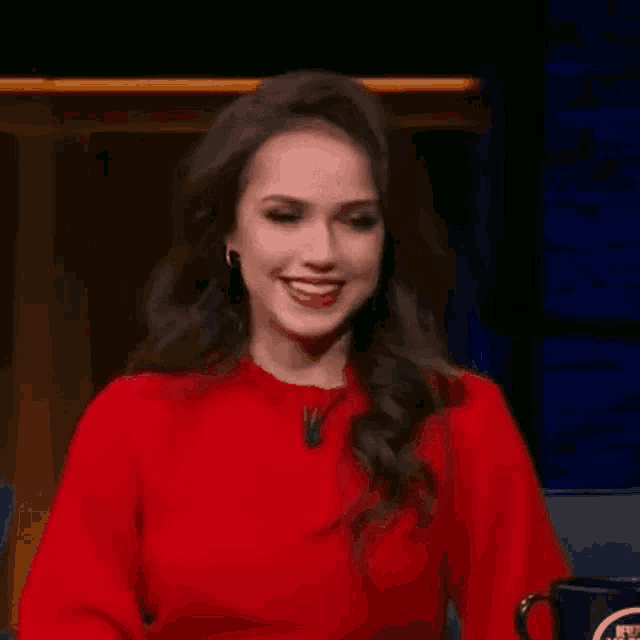 a woman in a red sweater is smiling while sitting in front of a blue mug .