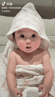 a baby is wrapped in a white blanket and holding a container of rice cream