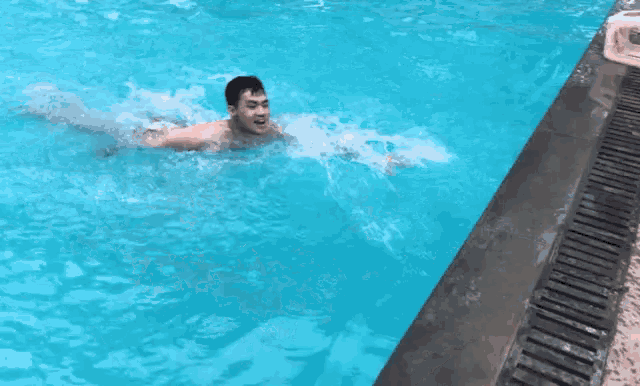 a man is swimming in a pool and reaching for the edge .