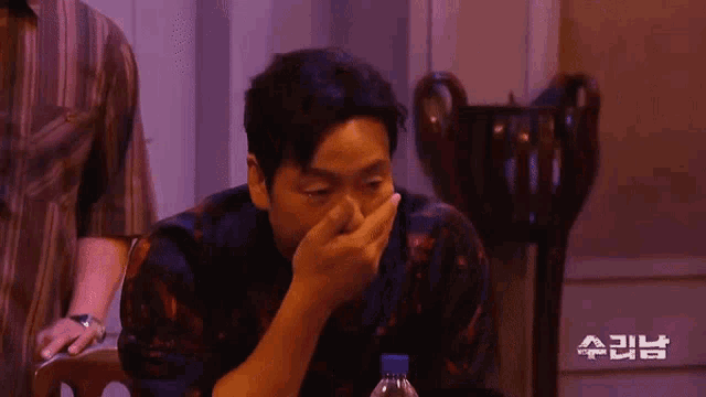 a man covering his mouth with his hand and a bottle of water