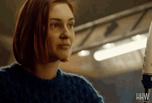 a woman in a blue sweater with the letters hw on the bottom right