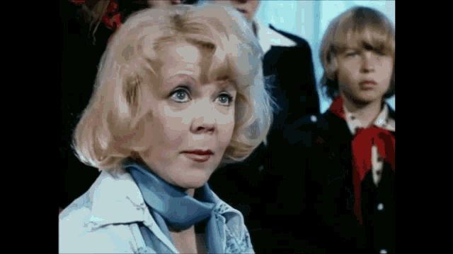a woman with blonde hair and a blue scarf around her neck is sitting in front of a group of children .