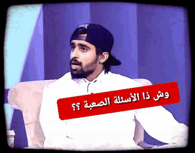 a man with a beard is sitting in a chair with a red sticker that says ' ? ' in arabic