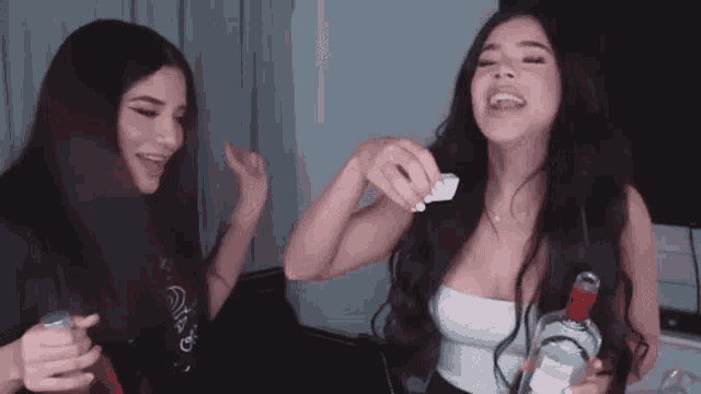 two women are sitting next to each other holding bottles of alcohol and drinking .
