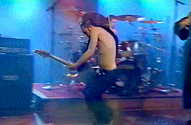 a shirtless man playing a guitar on a stage