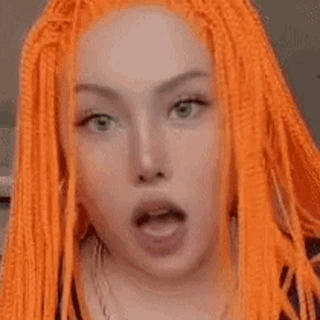a close up of a woman 's face with orange dreadlocks and a surprised look on her face .