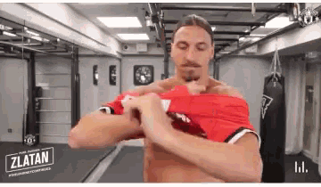 a man is taking off his shirt in a gym with a sign that says zlatan on it