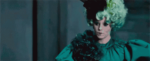 a woman in a green dress and green wig is standing in a dark room .