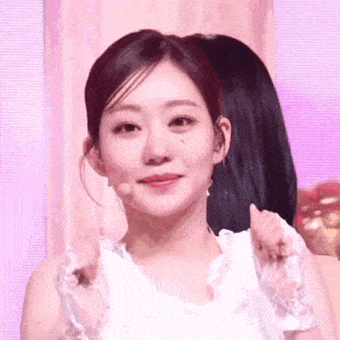 a woman in a white dress is making a heart shape with her hands .